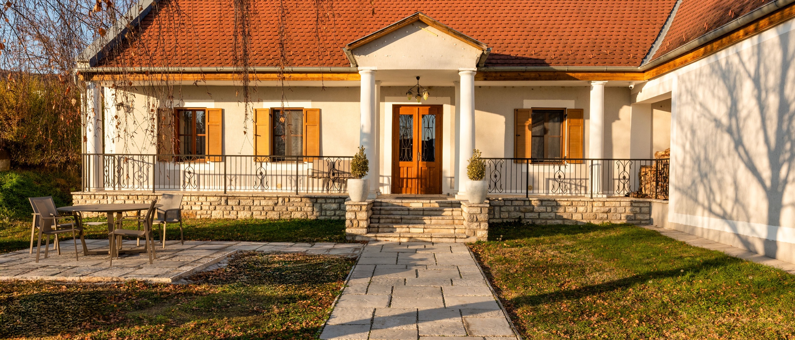 A kúria fehér falú, oszlopos tornácú főhomlokzata napfényben